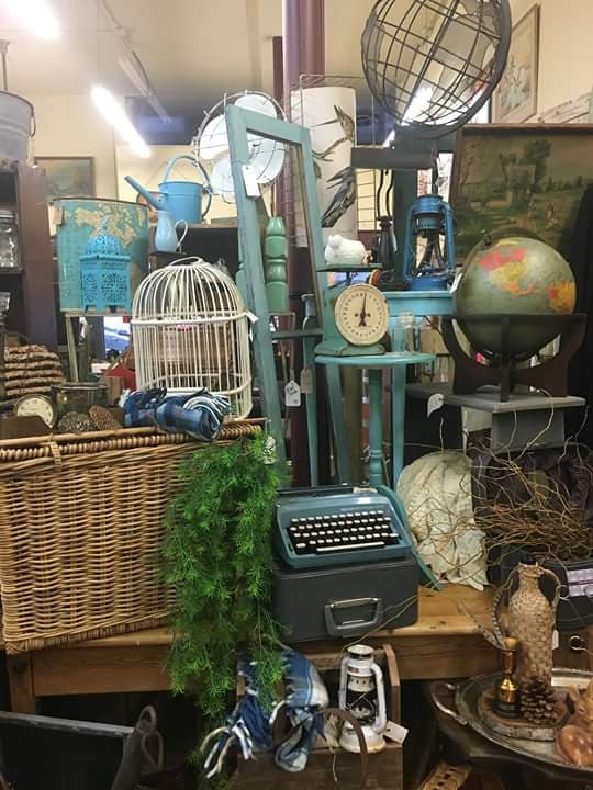 A booth packed with teal-painted vintage finds: birdcage, typewriter, lanterns, a globe, a watering can, and a wicker basket