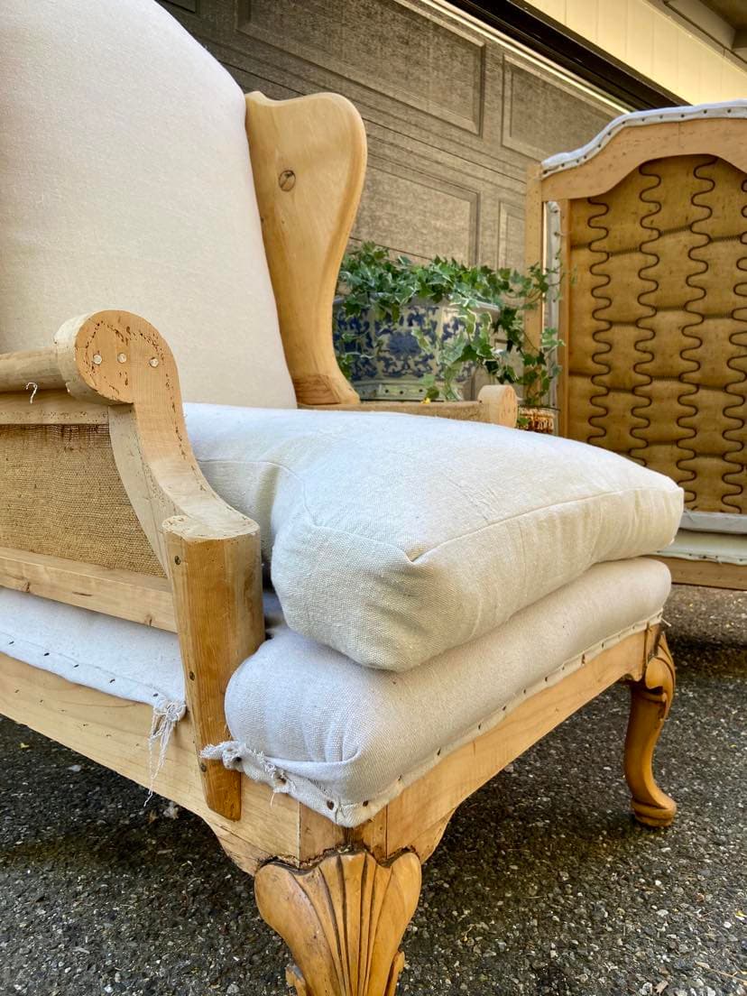 A deconstructed vintage wingback chair with natural linen upholstery and a bare wood frame, in Hadden Vintage Home’s European-inspired style